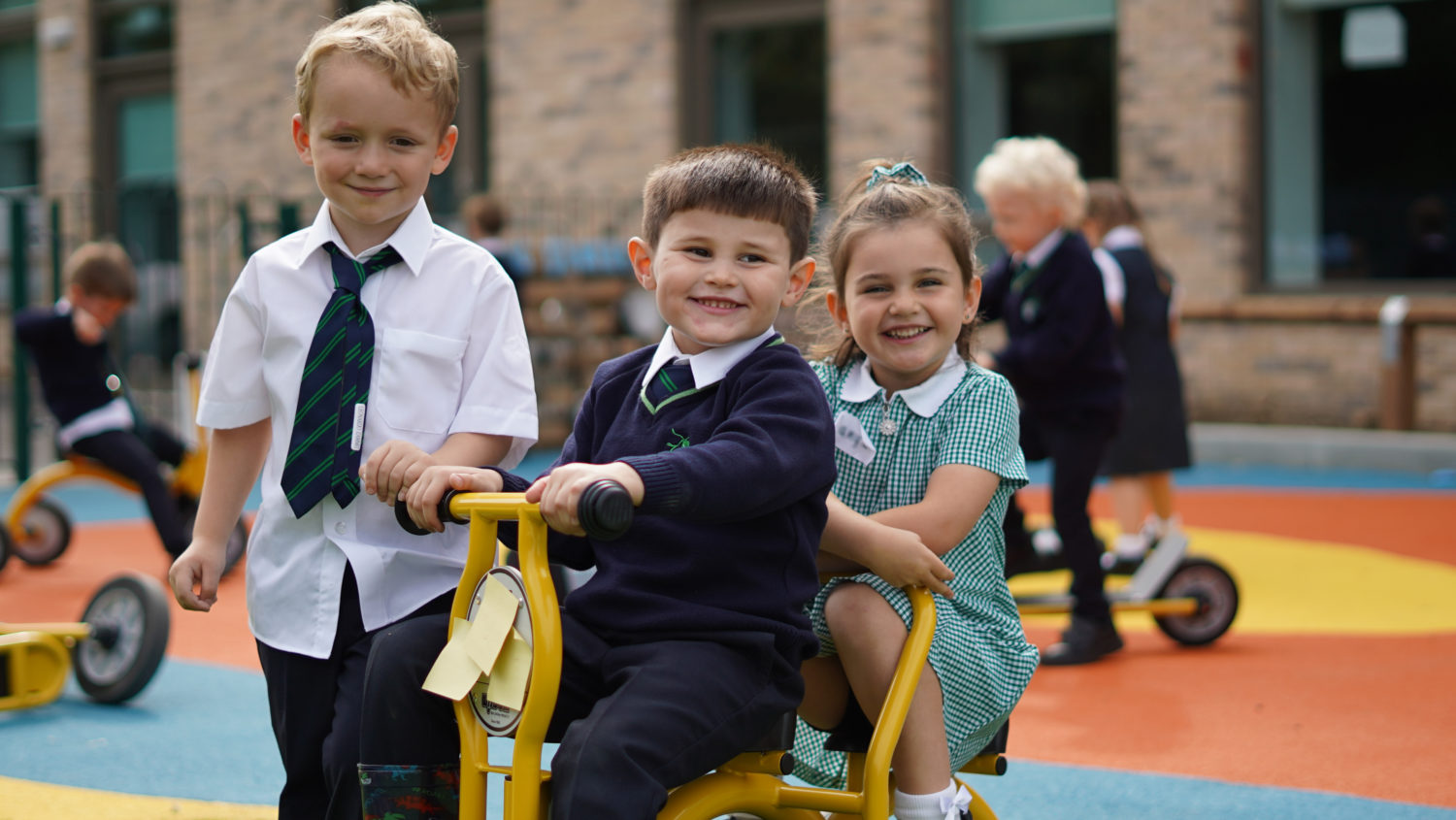 Children playing on the outdoor equipment, wearing their academy uniform and smiling brightly.