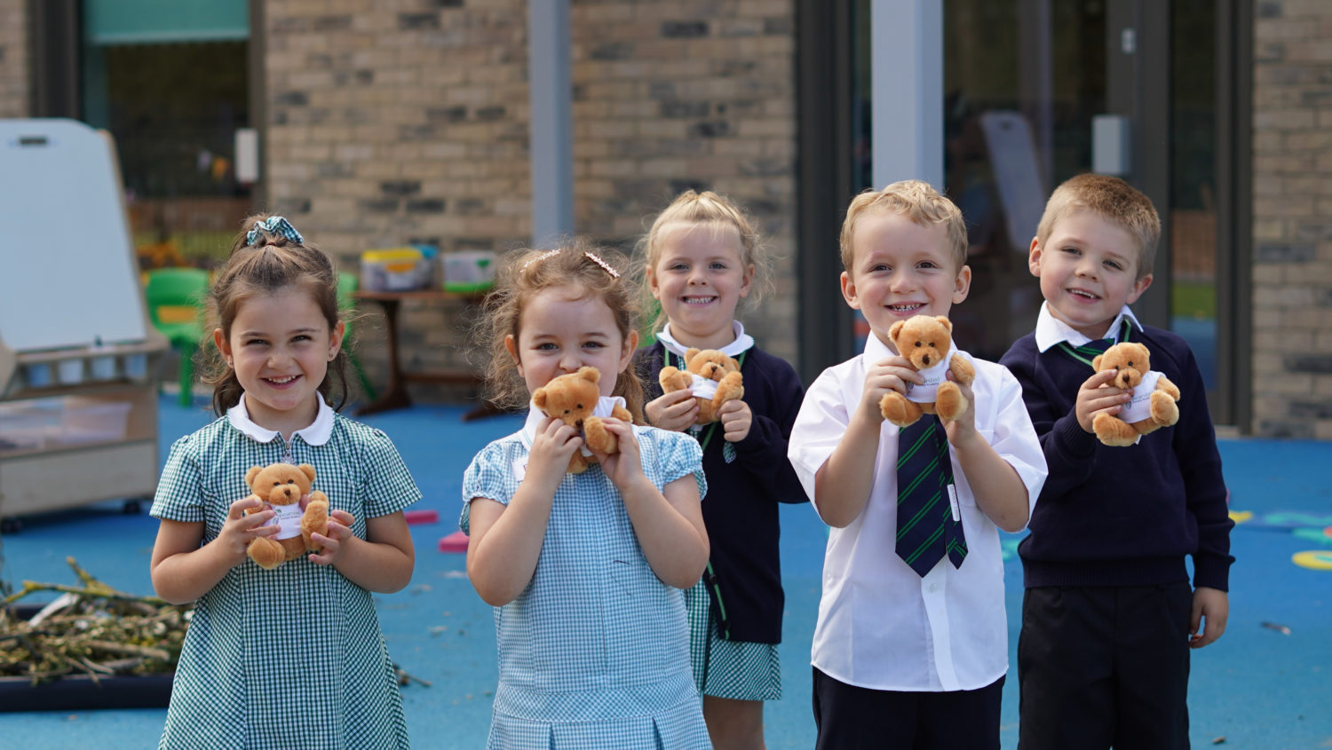 A small group of children holding teddy bears outside and smiling for the camera.