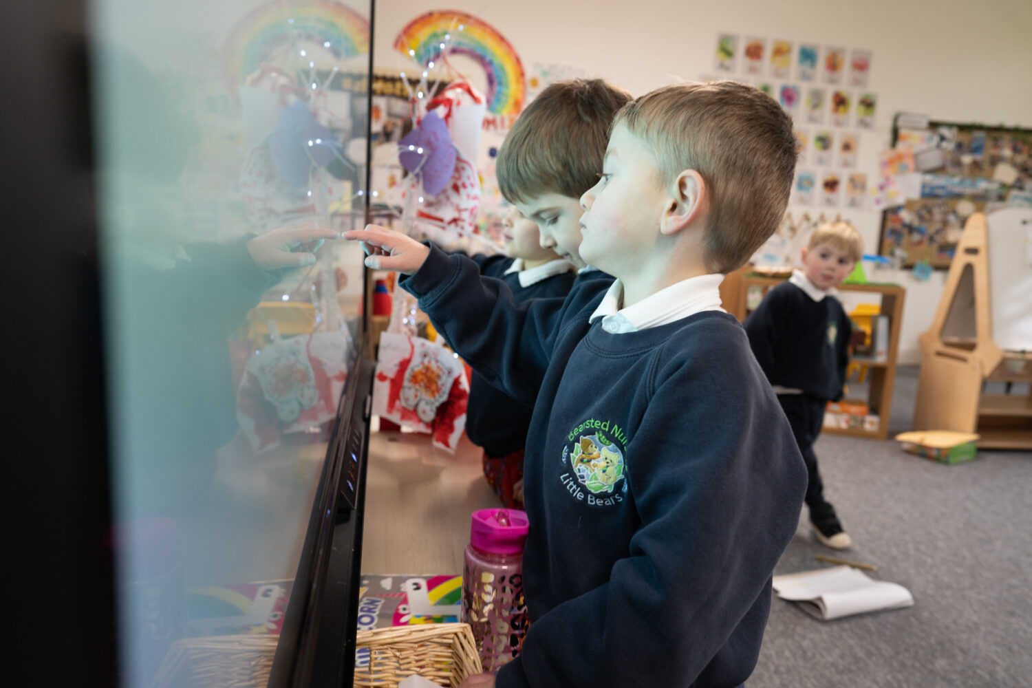 Three young boys from Nursery are pictured using the Interactive Board in their classroom to assist their learning.