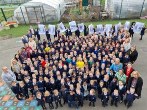 Lots of students from Bearsted Primary looking up at the camera. Students in the back row are each holding a sheet of A4 paper that reads out 'outstanding'